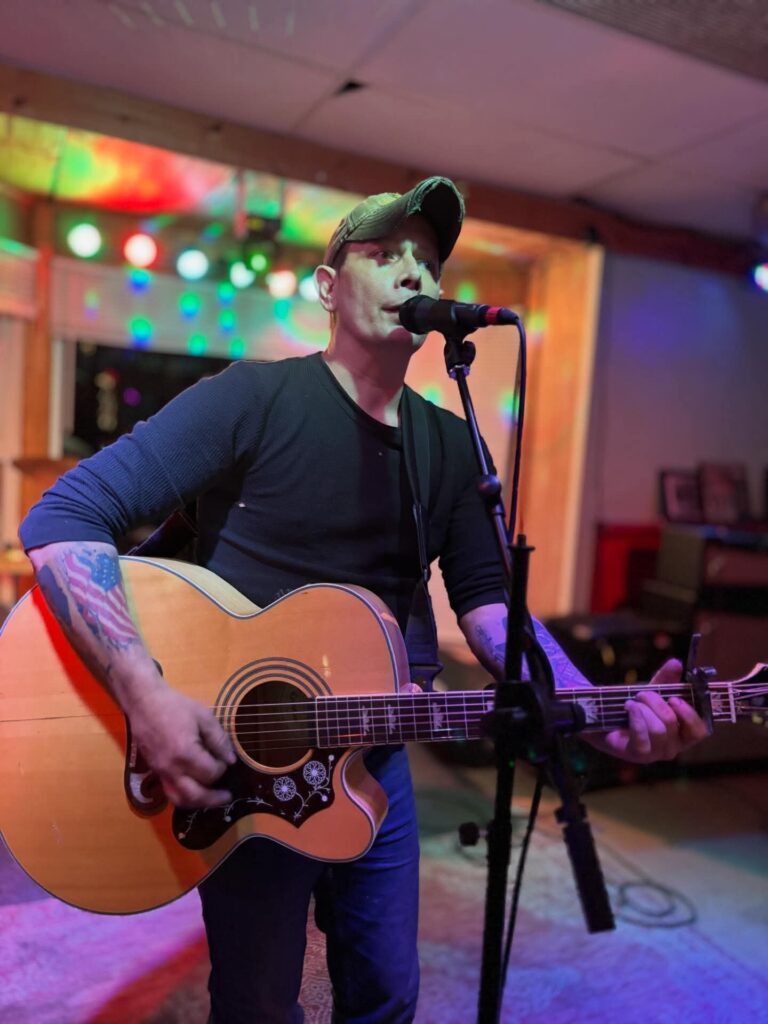 David Habian playing guitar and singing on stage under colorful lights